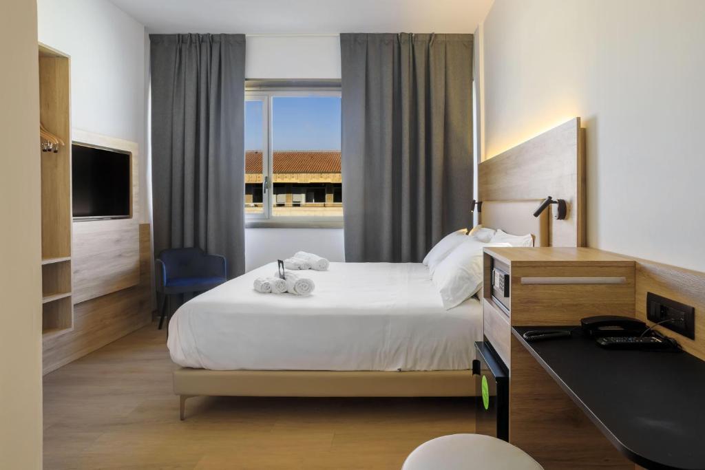 a hotel room with a bed with a desk and a window at B&B HOTEL Catania City Center in Catania