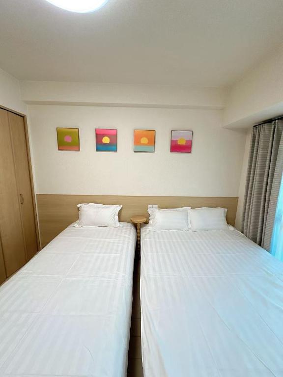 twee bedden in een kamer met schilderijen aan de muur bij katsu house 心斋桥 in Osaka