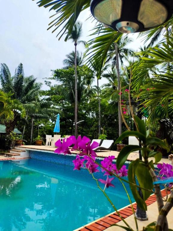 Una piscina en un resort con flores moradas y palmeras. en Baan WangNaKha, en Koh Samui