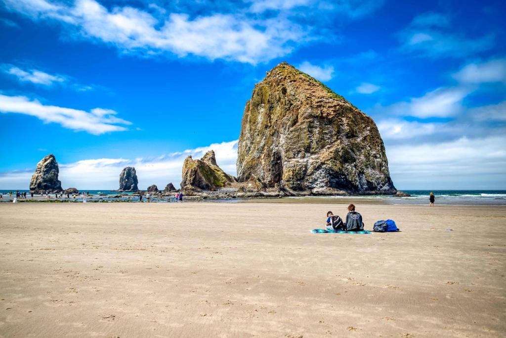 two people sitting on a beach with large rocks at Cannons Cottage in Cannon Beach