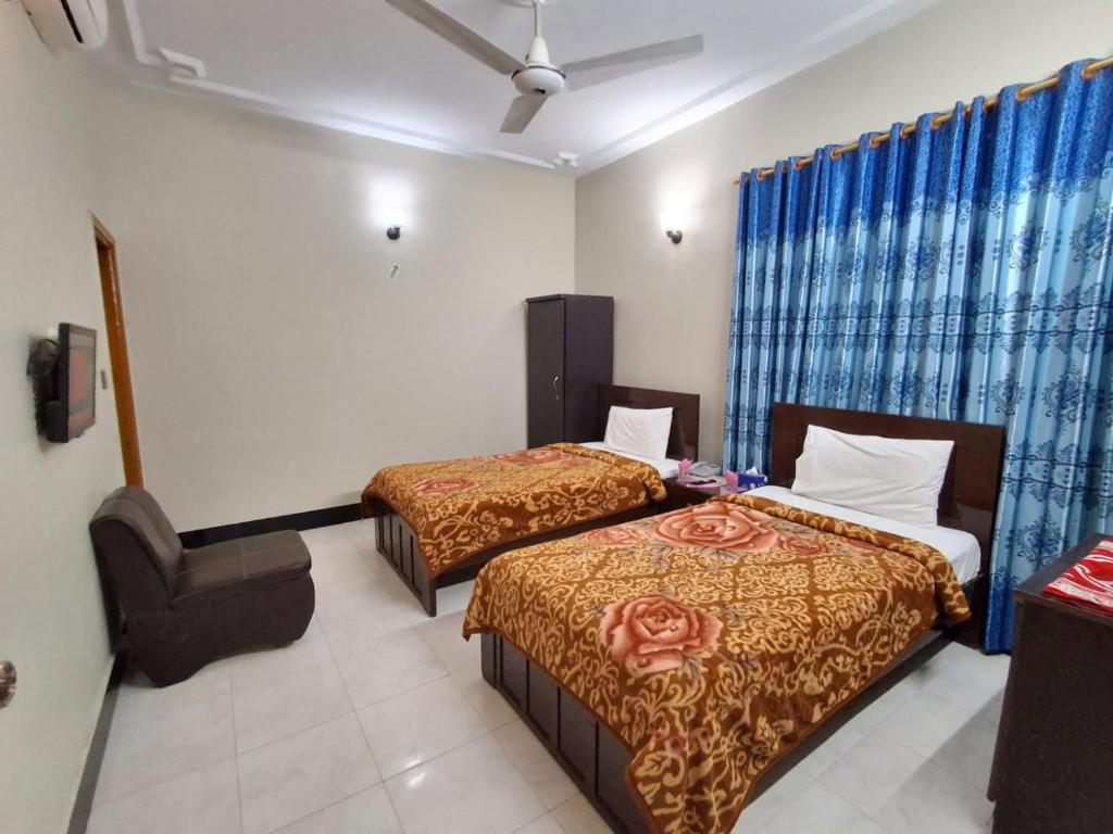 een hotelkamer met twee bedden en een stoel bij Rose Palace Guest House in Karachi