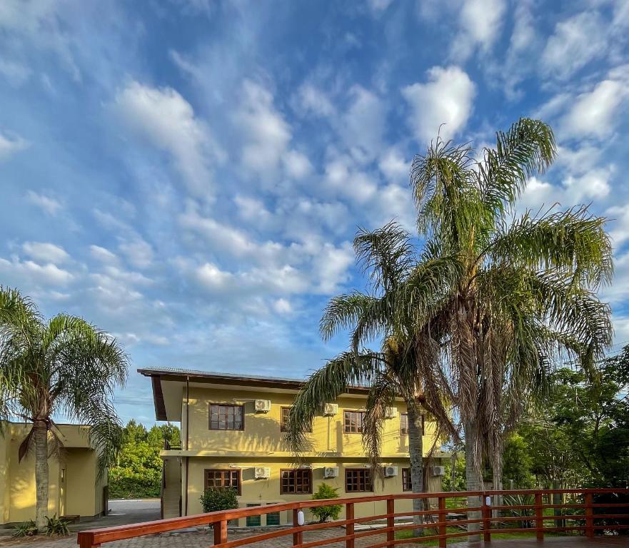 a yellow house with palm trees and a fence at Pousada Samburá in Garopaba
