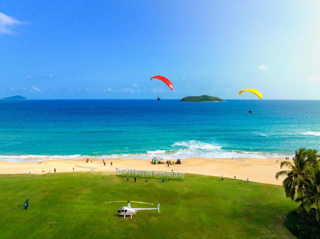 a group of people flying kites on a beach at The Westin Shimei Bay Resort in Wanning