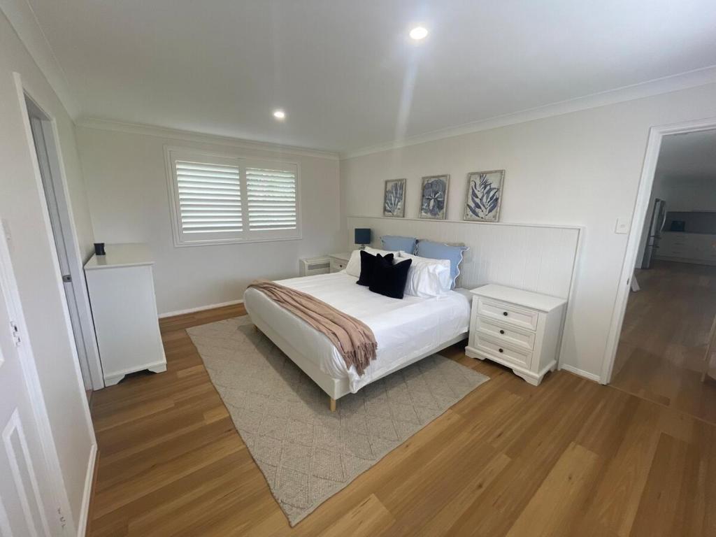 a white bedroom with a bed and a night stand at Coastal play and stay - walk to beach and park in Toowoon Bay
