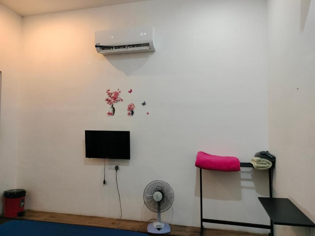 a room with a white wall with a fan and a tv at BENUTHOMEStay in Benut