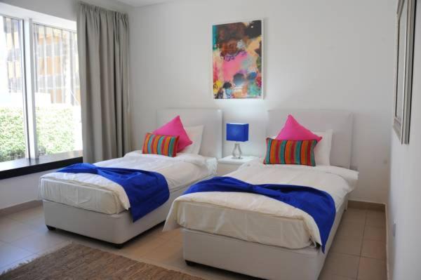 two beds in a bedroom with pink and blue pillows at Prime Hotel in Amman