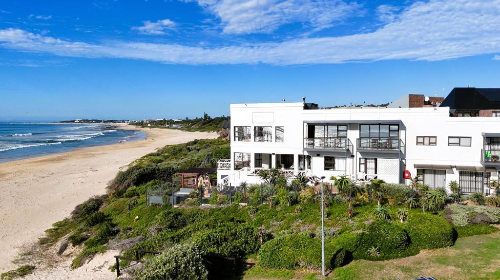 a white house on a hill next to a beach at On the Beach Guesthouse Jeffreys Bay in Jeffreys Bay