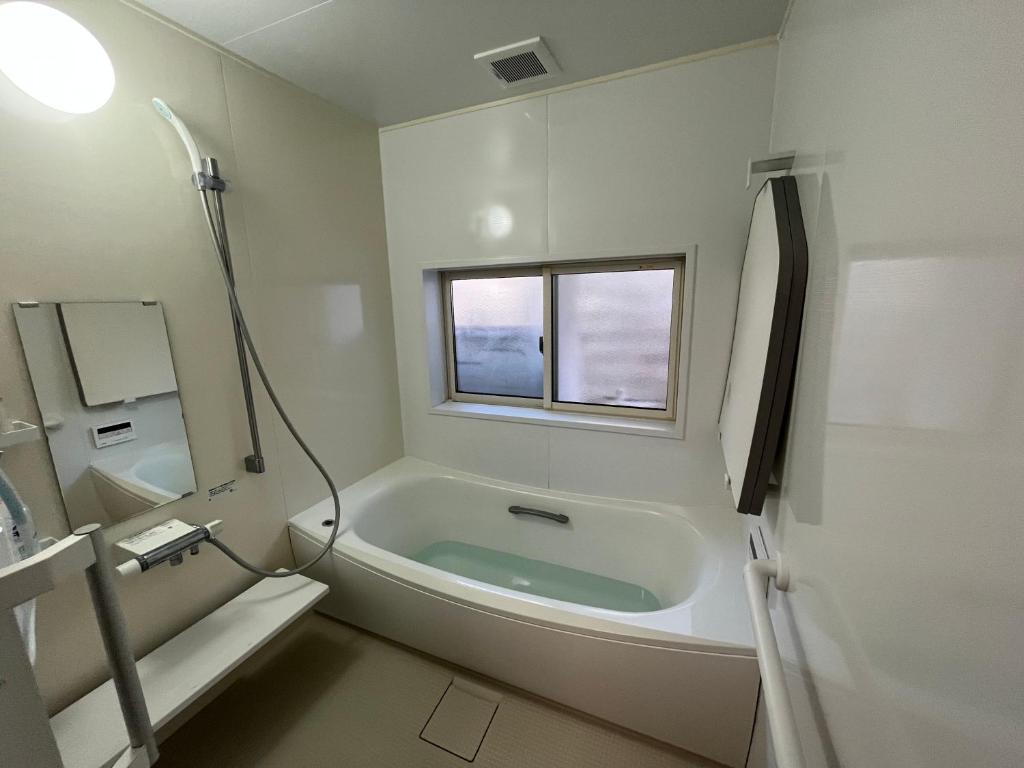 a white bathroom with a tub and a window at ゲストハウス椙乃家 in Matsukawa