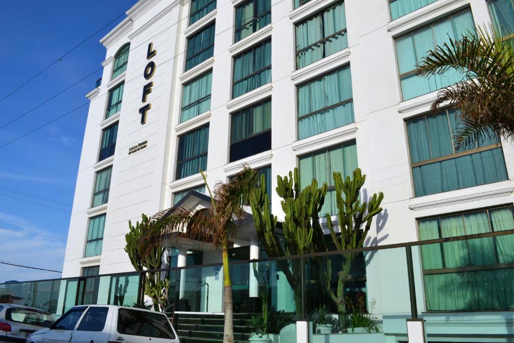 un edificio blanco con palmeras delante en Loft Prainha, en Arraial do Cabo