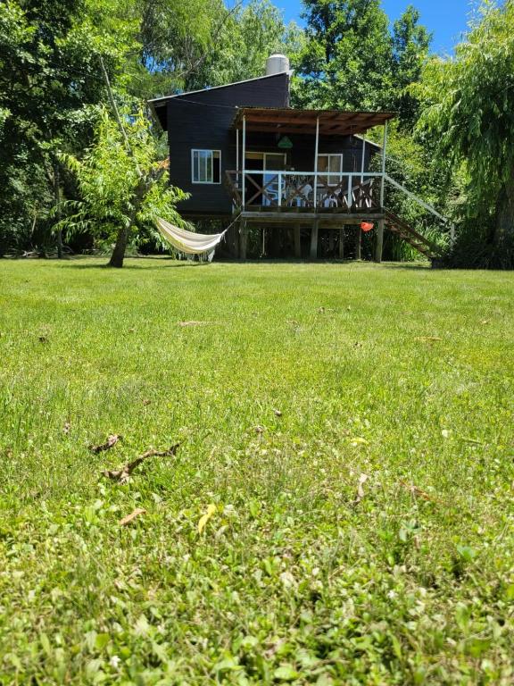 a house with a hammock in a field of grass at cabaña cuatro reinas in Tigre