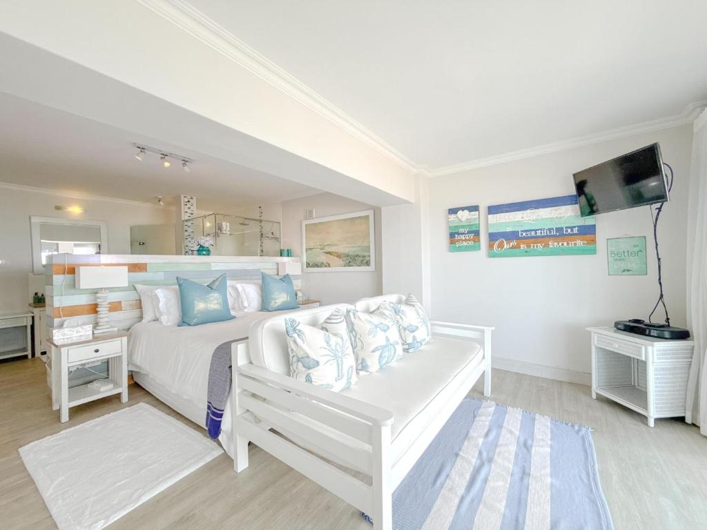 a white bedroom with a white bed and a couch at Harker Street Sea Facing Studio in Plettenberg Bay