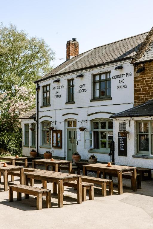 a group of wooden benches in front of a building at The Sun Inn At Hook Norton in Banbury