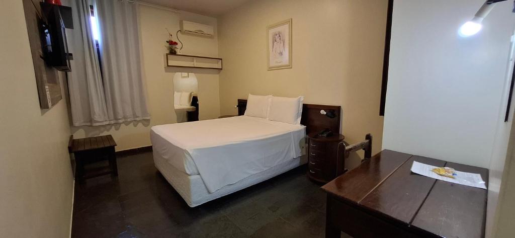 Un dormitorio con una cama blanca y un escritorio. en Hotel Monte Pascoal, en Itamaraju