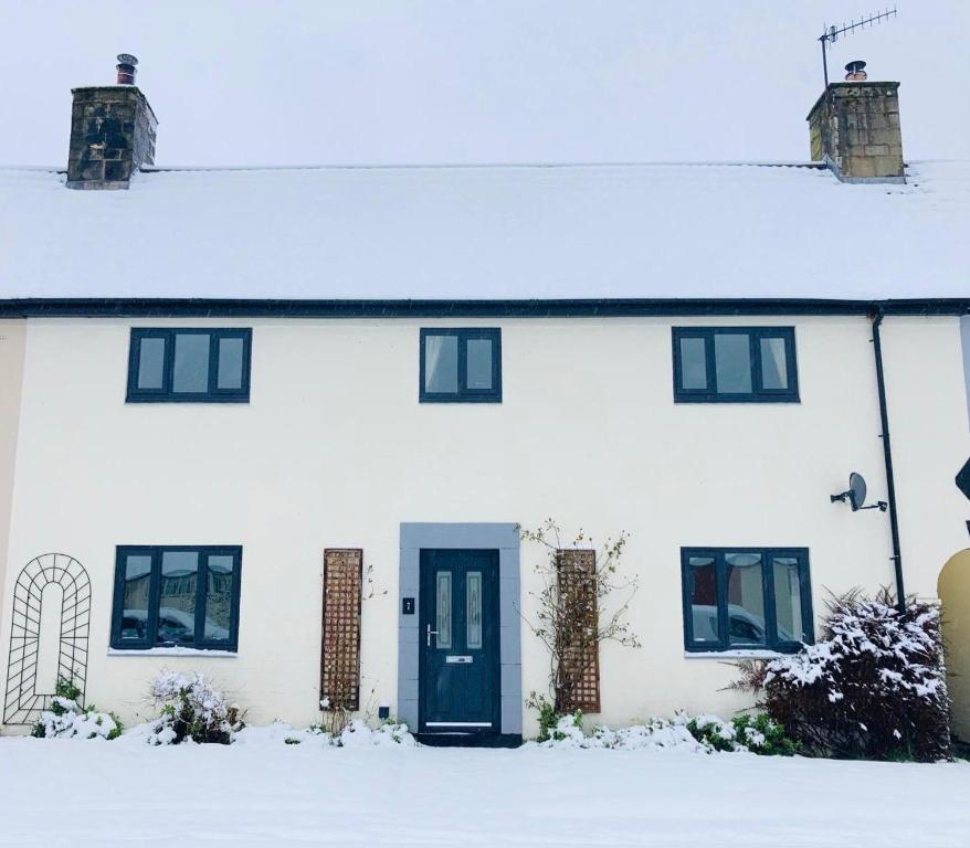 a white house with a blue door in the snow at Forest Retreat in Catcleugh