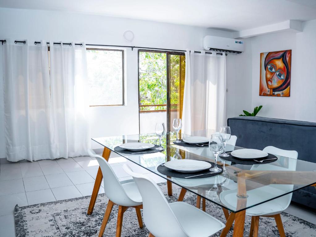 Appartement Cosy avec Balcon - Haie Vive في كوتونو: غرفة طعام مع طاولة زجاجية وكراسي بيضاء