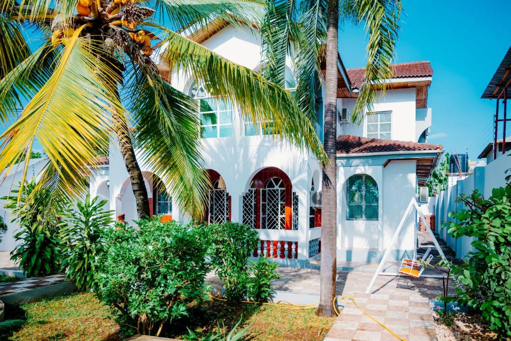 a white house with palm trees in front of it at Roots and Waves Apartment in Zanzibar City
