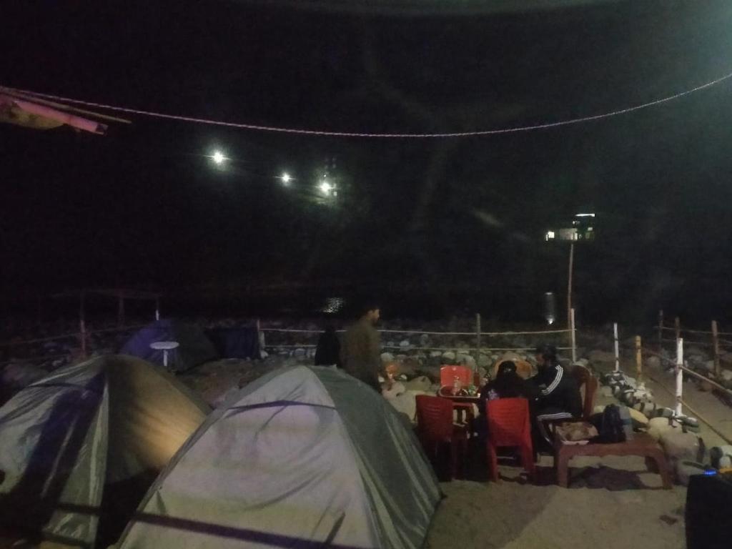 a group of people sitting around a tent at night at Rickson Riverside Campsite in Dawki