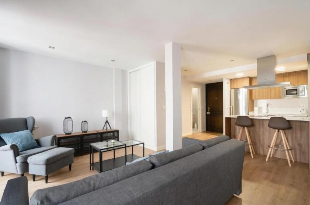 ein Wohnzimmer mit einer grauen Couch und einer Küche in der Unterkunft AVG Numa Guilhou 4 in Gijón