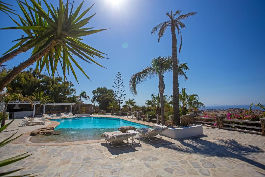 a swimming pool with lounge chairs and palm trees at Villa Scorpio by Bestofmikonos in Mikonos