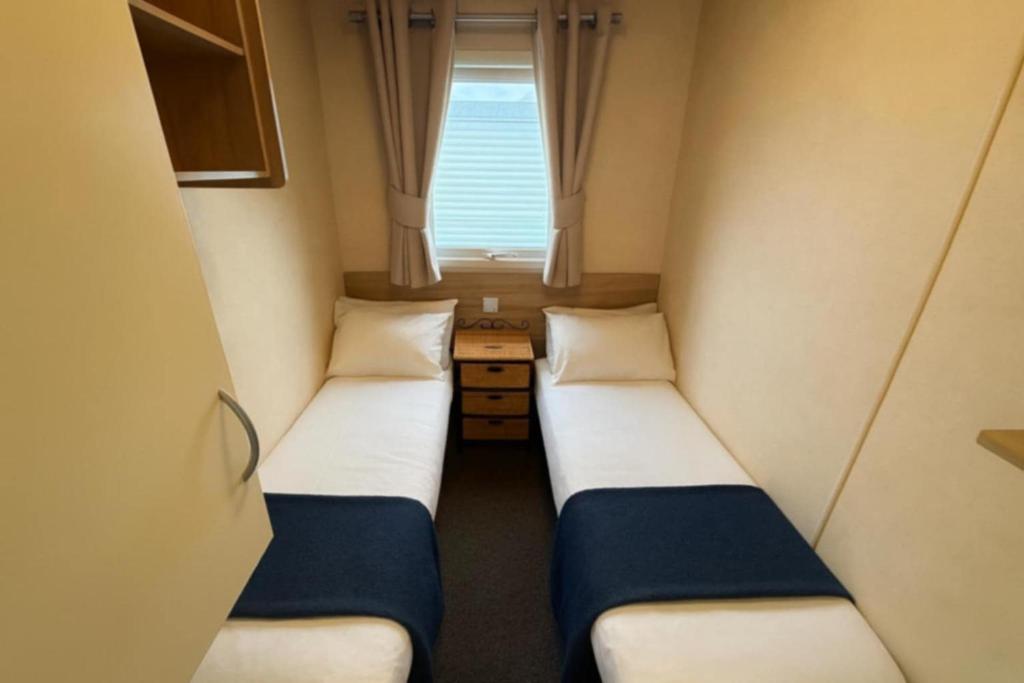 Dos camas en una habitación pequeña con ventana. en JTD golden gate caravan park towyn hire, en Kinmel Bay