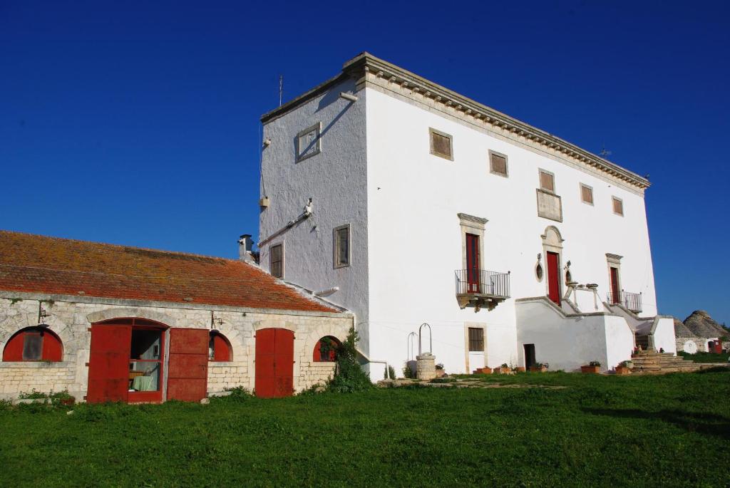 - un grand bâtiment blanc avec des portes rouges à côté d'un champ vert dans l'établissement Masseria Murgia Albanese, à Noci