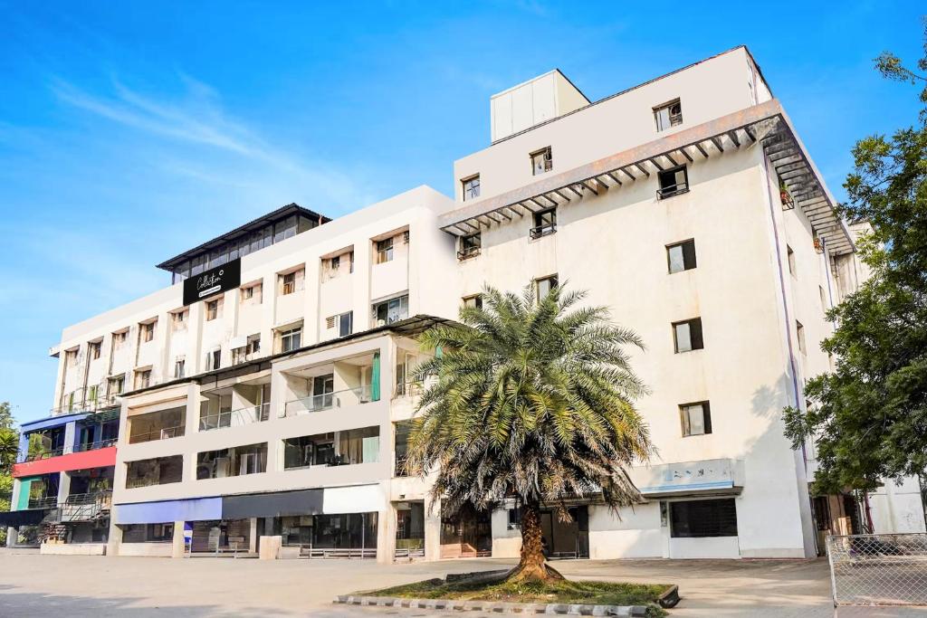 Un edificio blanco con una palmera delante. en Collection O Infocity Metro Station Gandhinagar Formerly Hotel LLP, en Gandhinagar