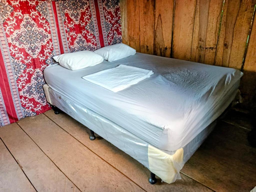un lit avec des draps blancs et des oreillers dans une chambre dans l'établissement Casa Del Árbol - Ometepe, à Santa Ana