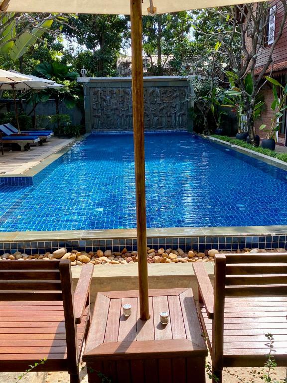a large swimming pool with two benches and an umbrella at Banksy's Siem Reap in Phumĭ Réach Born (2)