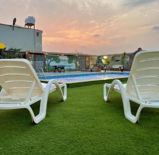 zwei weiße Stühle auf dem Rasen in der Nähe eines Pools in der Unterkunft VIP Villa in Quai