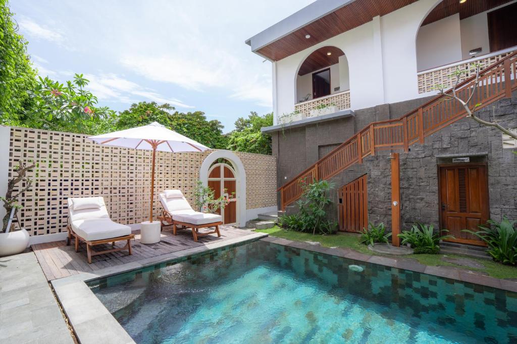 a house with a swimming pool and two chairs and an umbrella at Kania Rooms & Suite in Seminyak