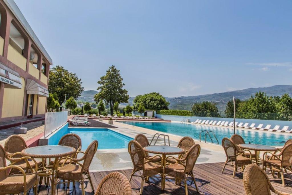 a pool with tables and chairs next to a building at Hotel Columbano in Peso da Régua