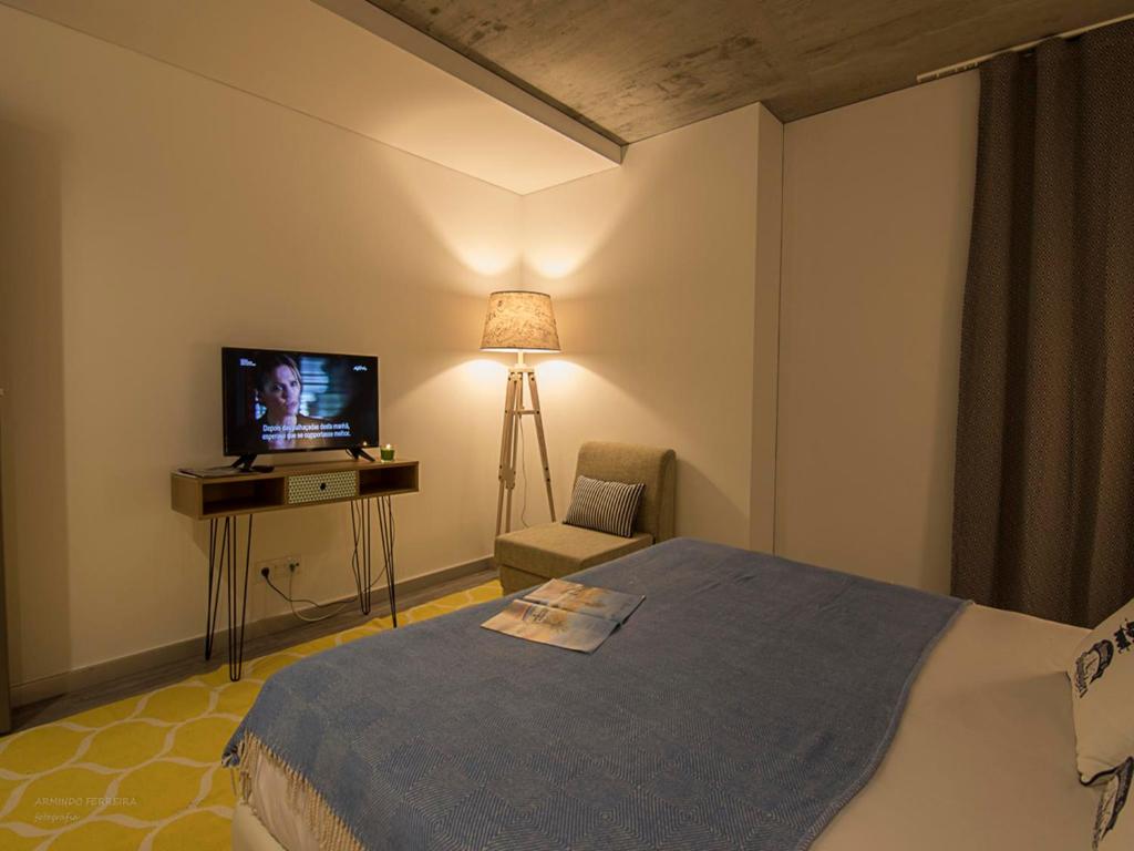 1 dormitorio con 1 cama, TV y silla en S. Gonçalinho - Suites Apartments, en Aveiro