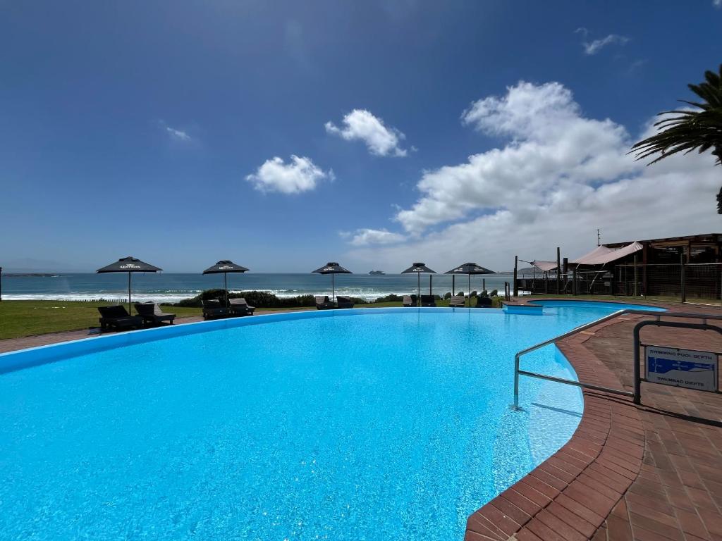 een groot blauw zwembad met de oceaan op de achtergrond bij Coastal Hospitality - Beach Club 205 in Mosselbaai