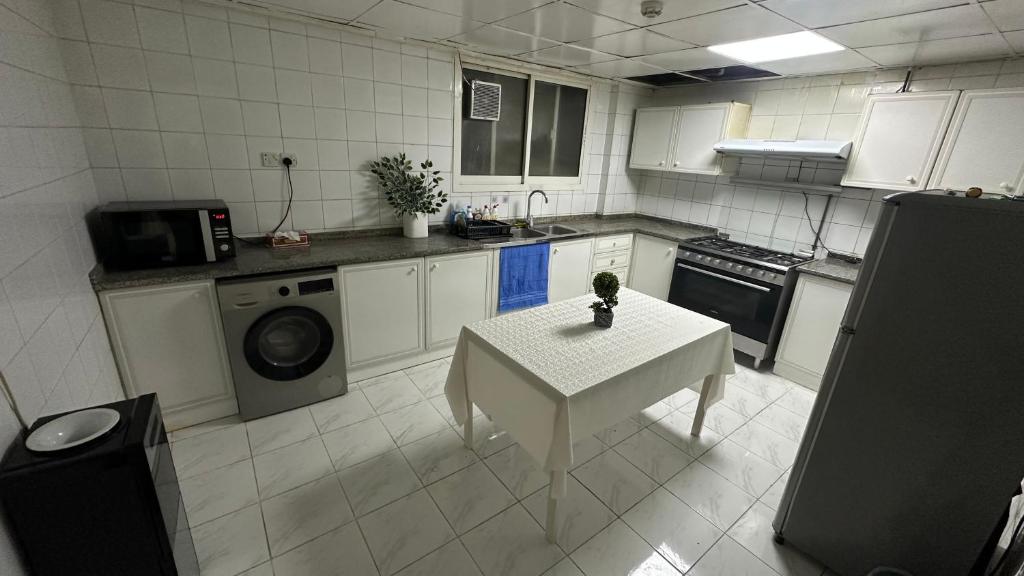 a kitchen with a table and a sink and a washing machine at Single bed space - Al Majaz 2 in Jazīrat al Ḩibāb