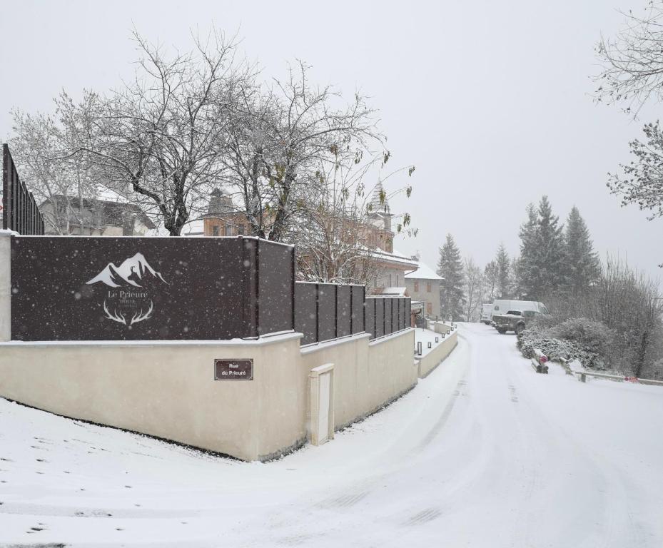 una calle cubierta de nieve con una valla y árboles en Hôtel Le Prieuré - Pra Loup 1500, en Pra-Loup