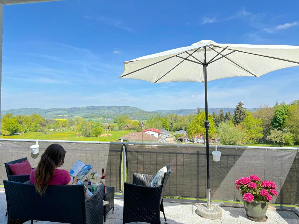 a woman sitting in a chair under an umbrella at Ferien am Winkelhof in Deggenhausertal