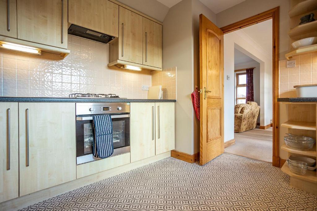a kitchen with wooden cabinets and an open door at Sparrows - Crail in Crail
