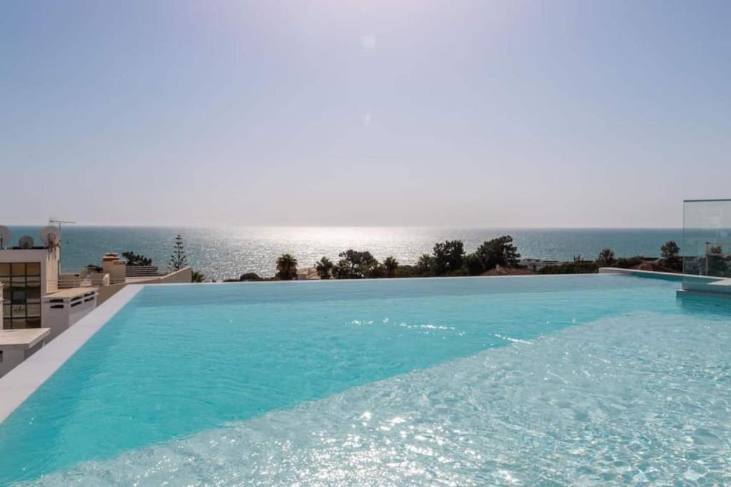 a large swimming pool with the ocean in the background at New 2bedroom Apartment w Terrace & Infinity Pool in Olhos de Água