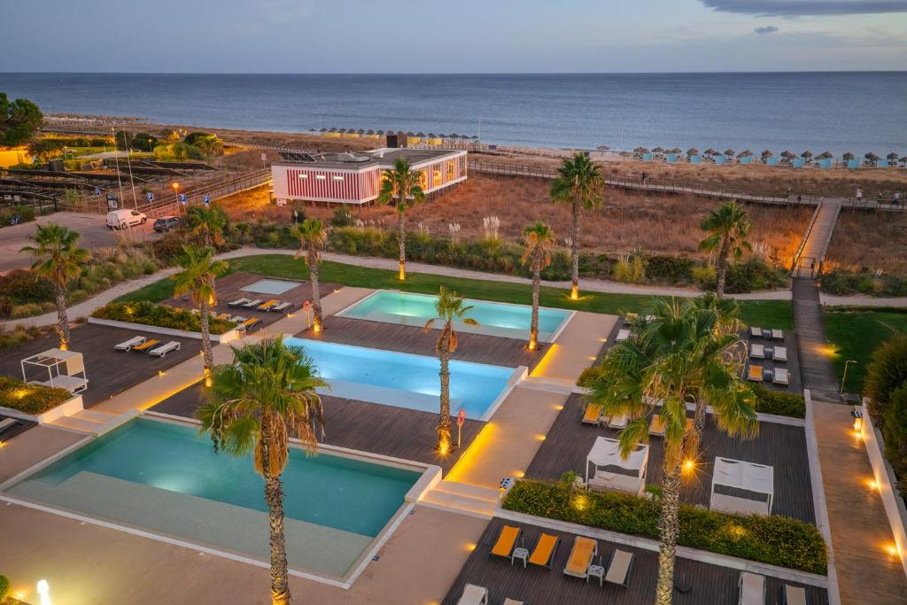 Pestana Alvor South Beach Premium Suite Hotel في ألفور: اطلالة جوية على منتجع فيه نخيل والمحيط