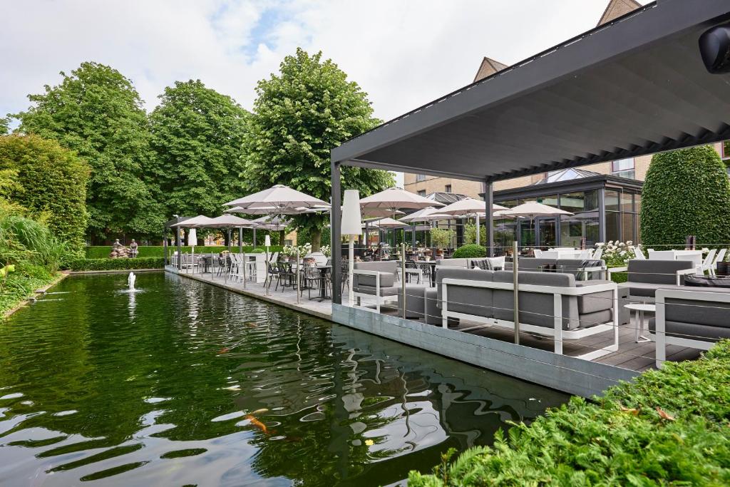 un restaurante con mesas y sillas junto a un estanque en Ariane Hotel, en Ypres