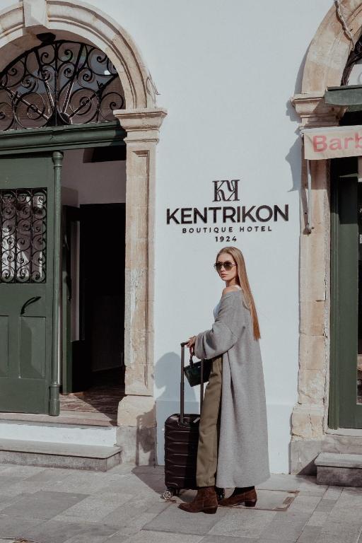 Una mujer parada frente a un edificio con una maleta. en Kentrikon 1924 Boutique Hotel, Old Town, en Pafos