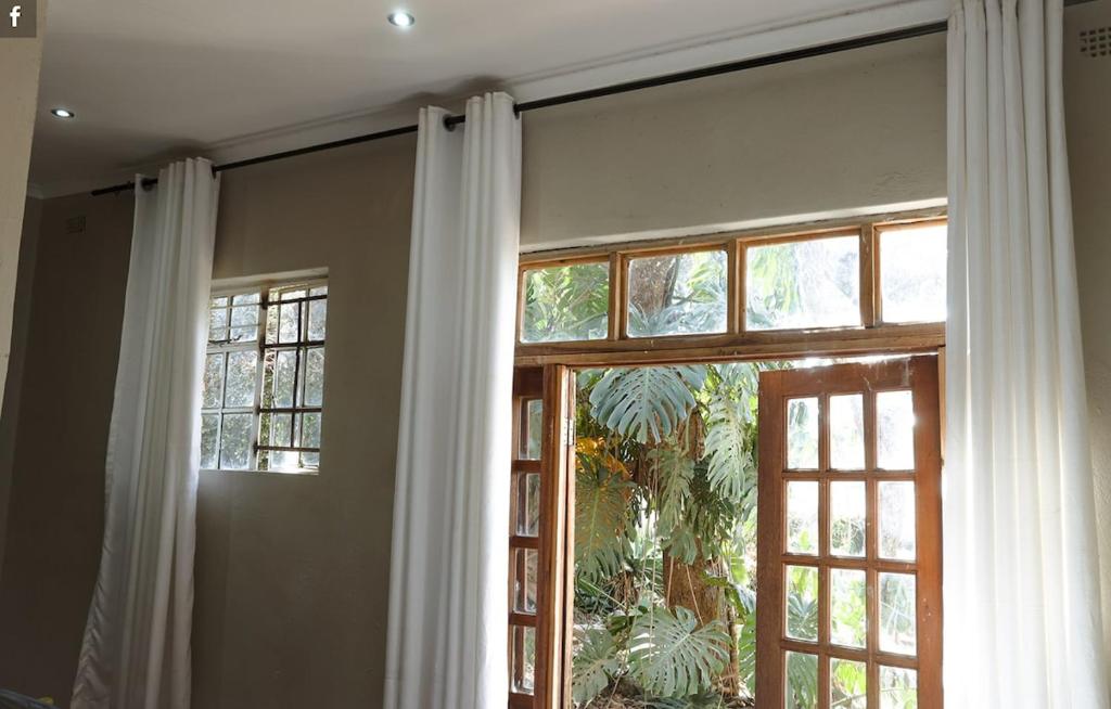 ein Fenster mit weißen Vorhängen in einem Zimmer in der Unterkunft Cozy Ensuite Borrowdale in Harare