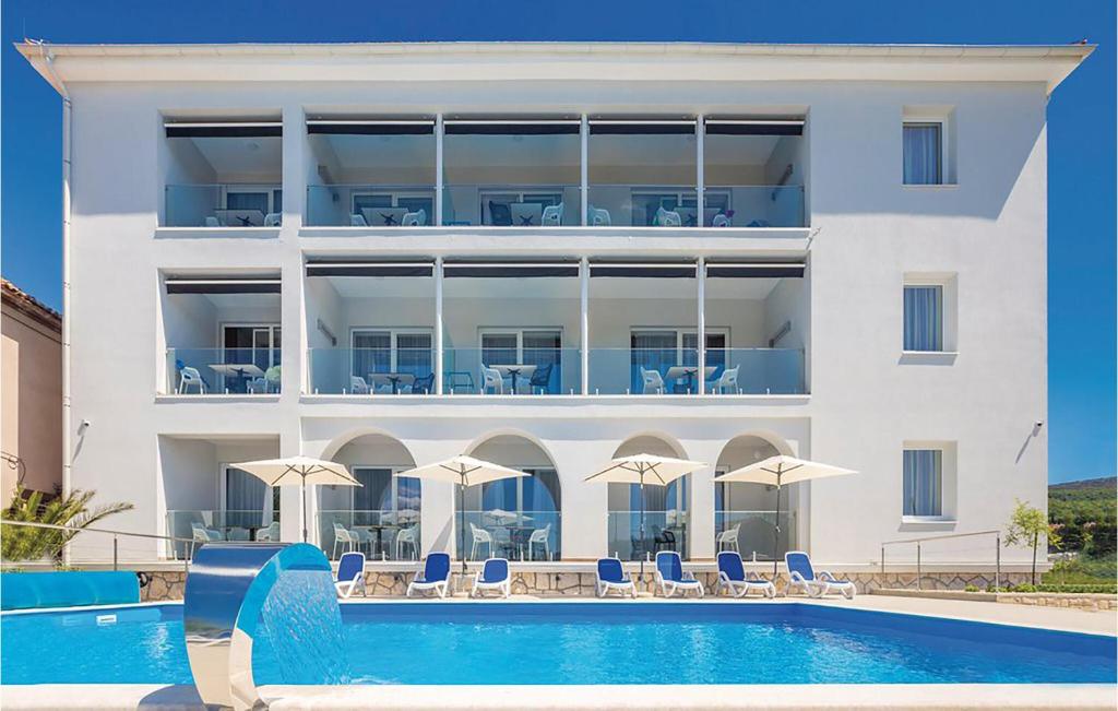 un grande edificio bianco con piscina, sedie e ombrelloni di 2 Bedroom Awesome Apartment In Punat a Punat