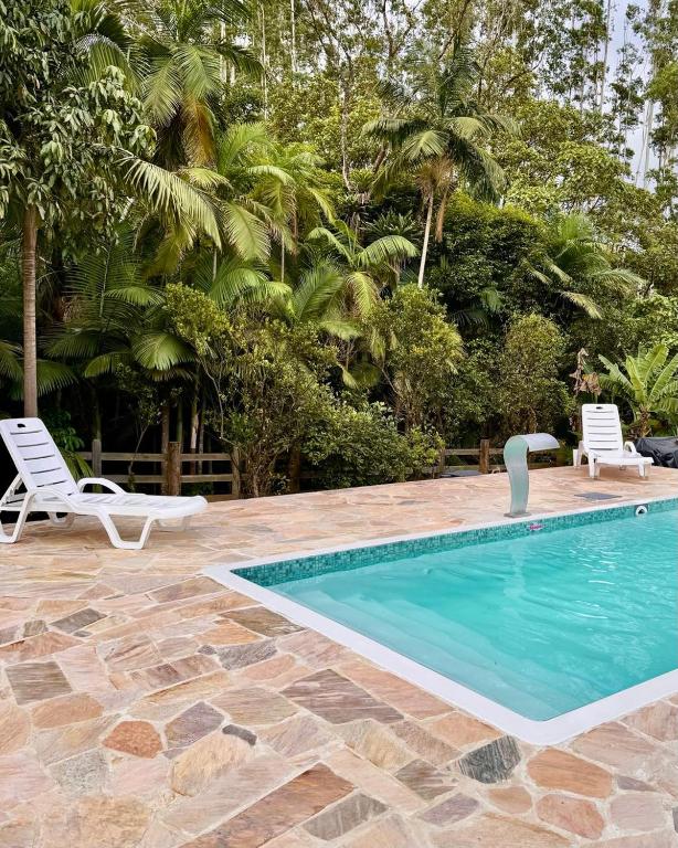 a swimming pool with two white chairs next to a resort at Sítio Feltz in Canelinha