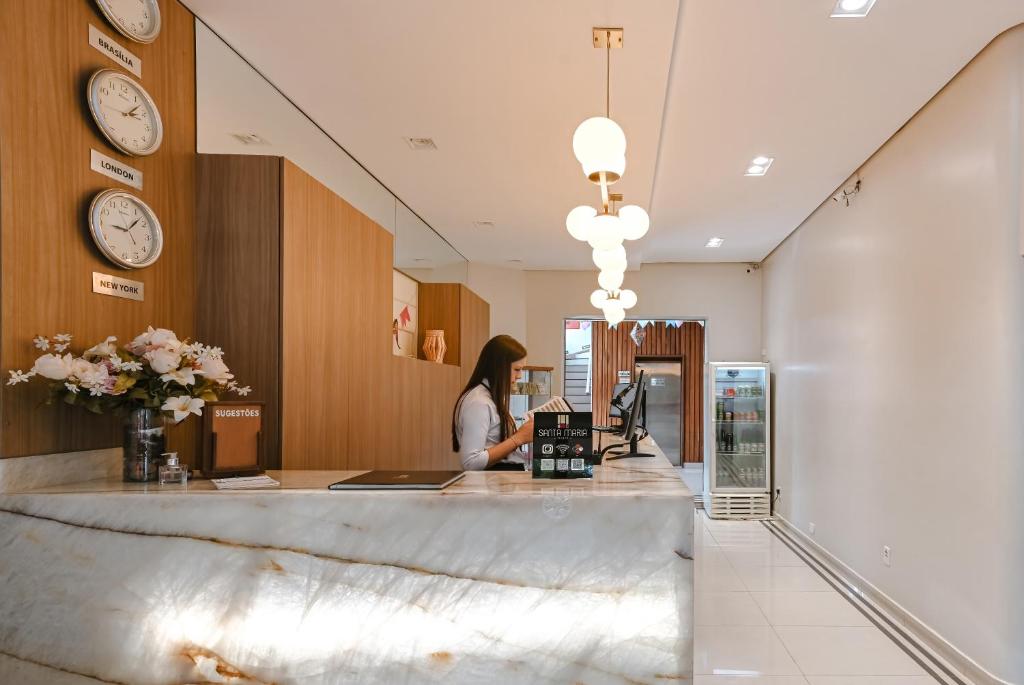 a woman standing at a counter in a store with clocks at Hotel Santa Maria in Campo Mourão