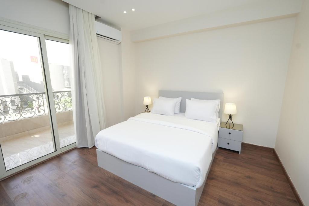 ein weißes Schlafzimmer mit einem Bett und einem großen Fenster in der Unterkunft Settle Inn Banafseg Apartments in Kairo