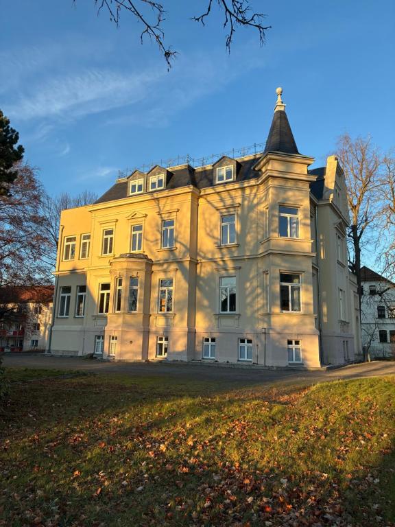 ein großes gelbes Gebäude mit einem Turm oben in der Unterkunft MartiniVilla Rooms in Glauchau