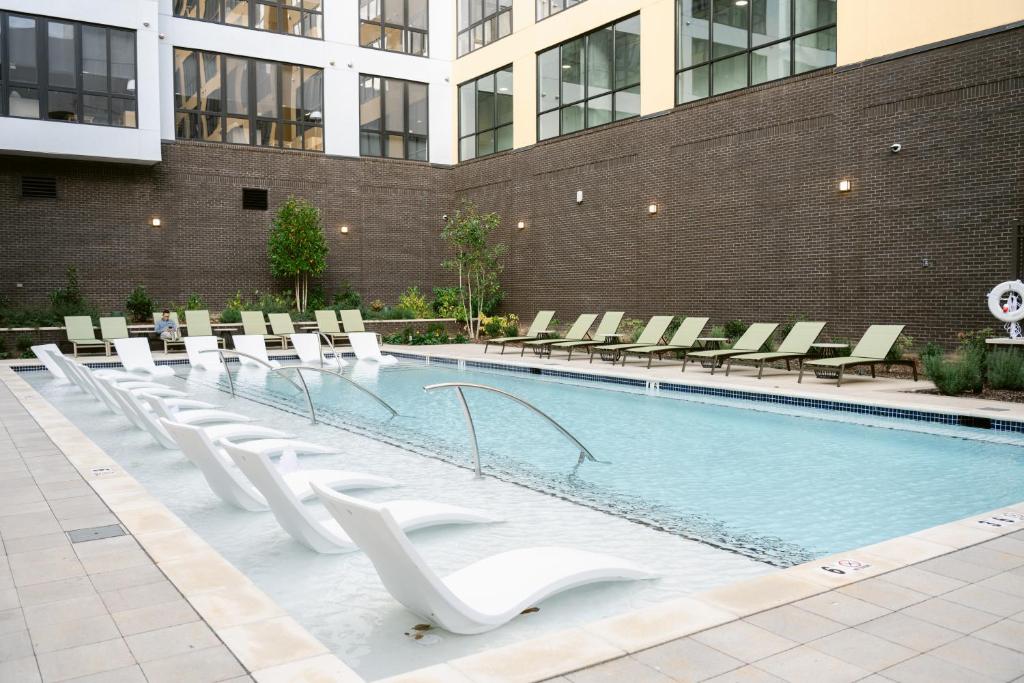 ein Pool mit weißen Stühlen und ein Gebäude in der Unterkunft Placemakr Huntsville - MidCity District in Huntsville