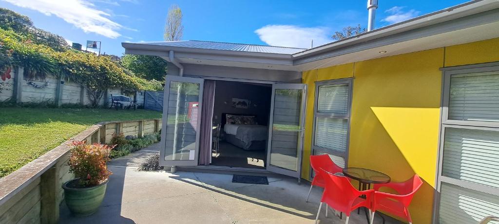 una casa amarilla con dos sillas rojas y una mesa en Hidden Gem in Oaklands, en Napier