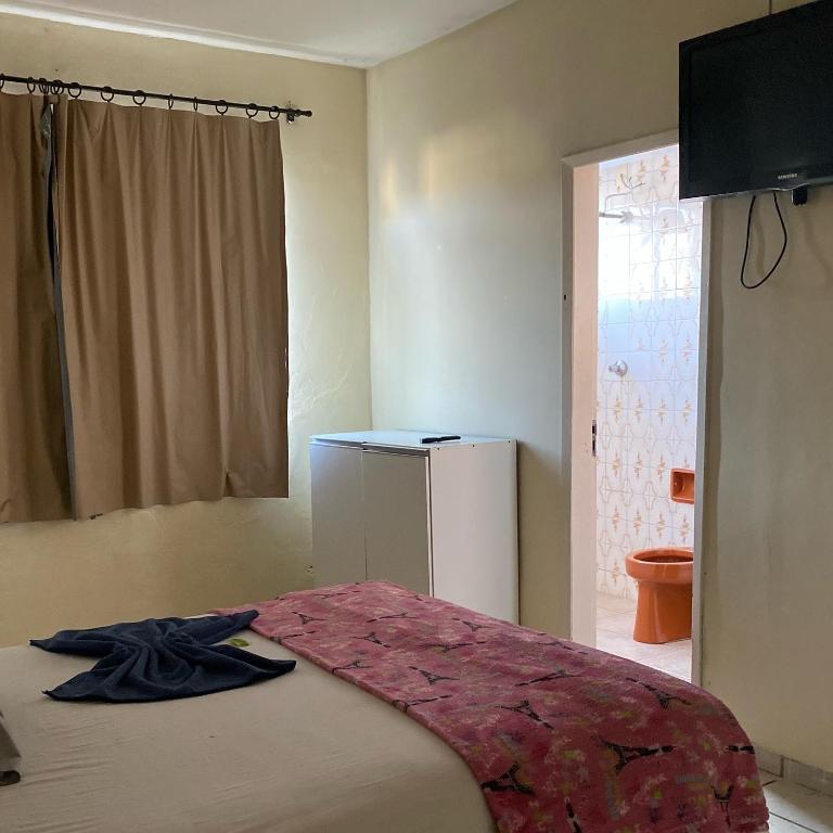 a bedroom with a bed and a refrigerator and a window at Quarto econômico no centro in Sete Lagoas